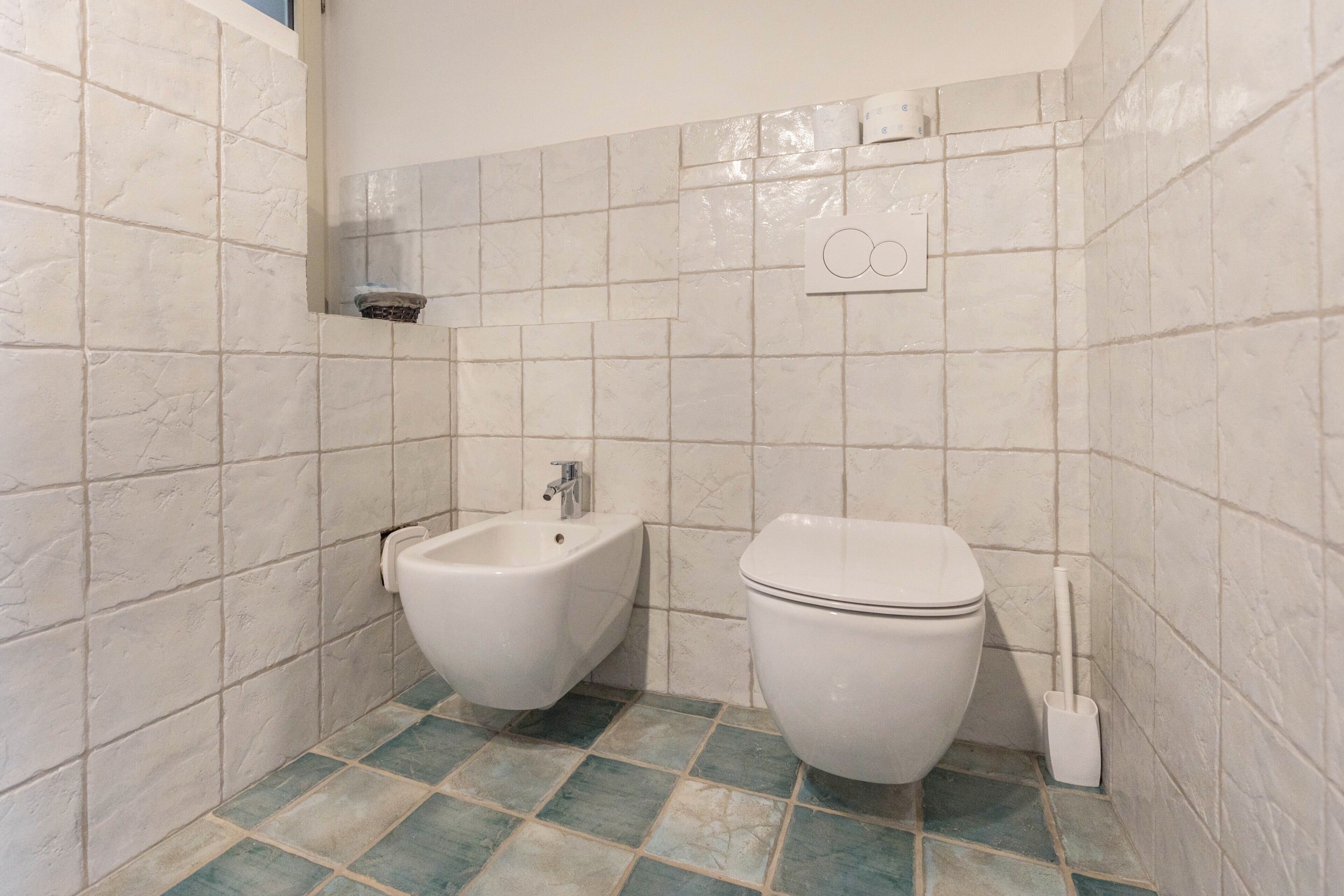 Un baño con bidé, inodoro y piso de baldosas.
