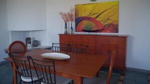 A dining area with a wooden table and chairs, a colorful abstract painting, and a white wall. - Villa 'Maria' with Sea View, Private Terrace and Wi-Fi (Cala Liberotto)