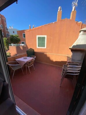 Une terrasse avec une table et des chaises, une petite fenêtre et un mur rouge.