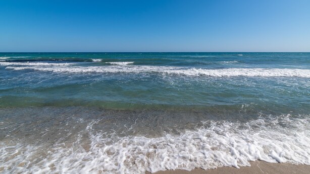 A beach with clear blue water and waves.