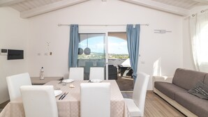 A dining area with a table set for two, a sofa, and a view through a glass door to the outside.
