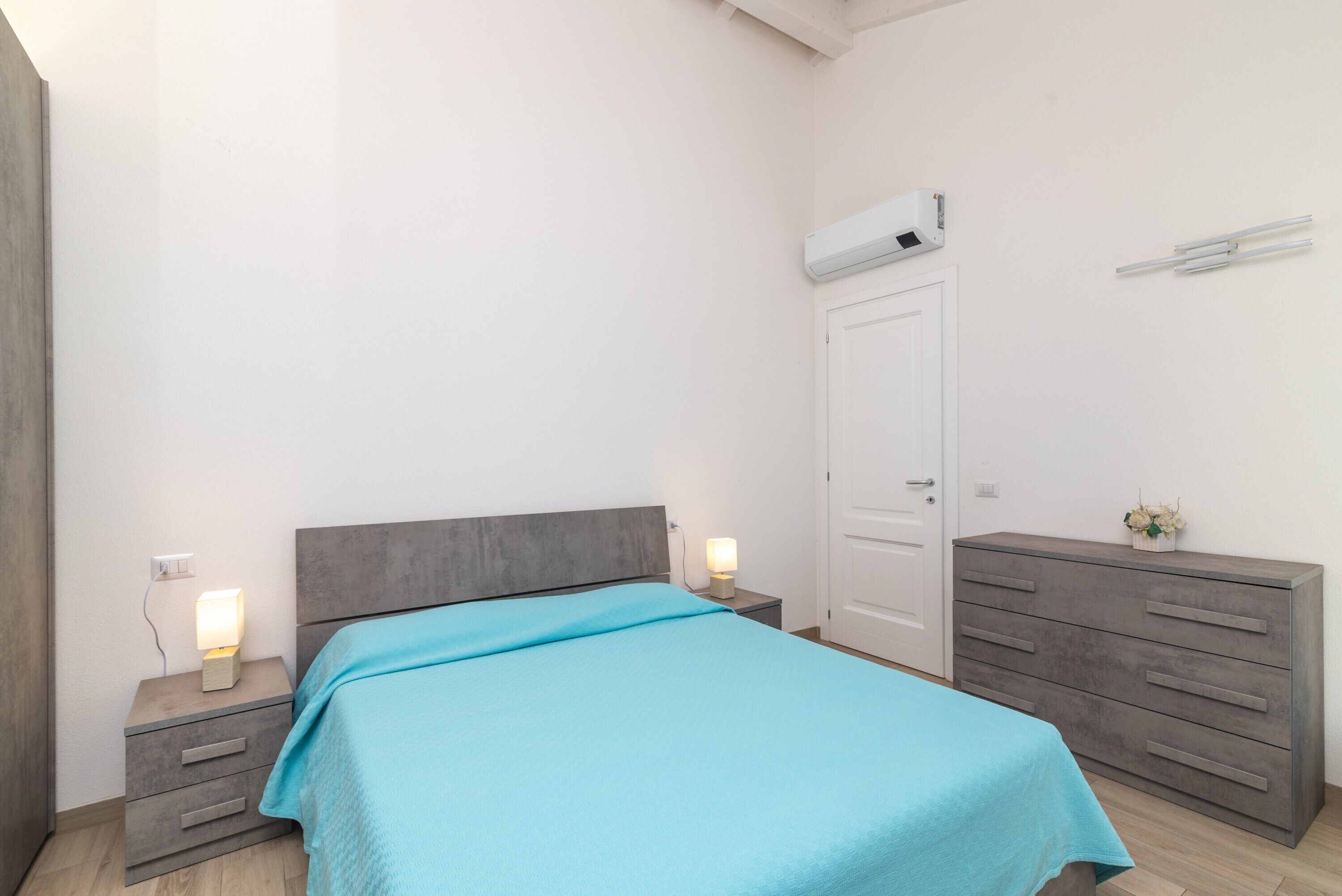 Een slaapkamer met een bed, nachtkastjes, een dressoir, een airconditioner en een deur.