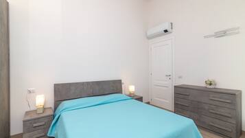 Een slaapkamer met een bed, nachtkastjes, een dressoir, een airconditioner en een deur.