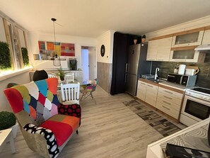 Cozinha moderna com geladeira, micro-ondas e forno. Possui uma área de refeições com um sofá e cadeiras coloridas.