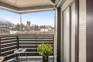 Un balcón con planta en maceta, una mesita y una vista a un castillo a lo lejos.