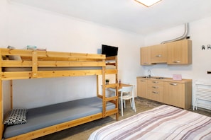 Una cama litera con escritorio y silla, una pequeña cocina y un radiador.