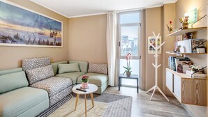 Ein Wohnzimmer mit einer Couch, einem kleinen Tisch, einem Bücherregal und einem großen Fenster.
