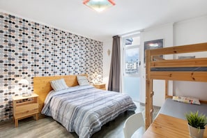 Un dormitorio con cama, mesita de noche, lámpara y vistas a la ciudad a través de una ventana.