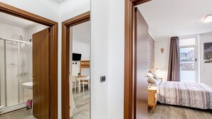 Une chambre comprenant un lit, un bureau, une chaise, une fenêtre avec des rideaux et une salle de bain avec une douche et un lavabo.