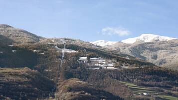 Eine gebirgige Landschaft mit einer Ansammlung von Gebäuden, möglicherweise ein Resort oder eine Lodge, umgeben von bewaldeten Hügeln und schneebedeckten Gipfeln.
