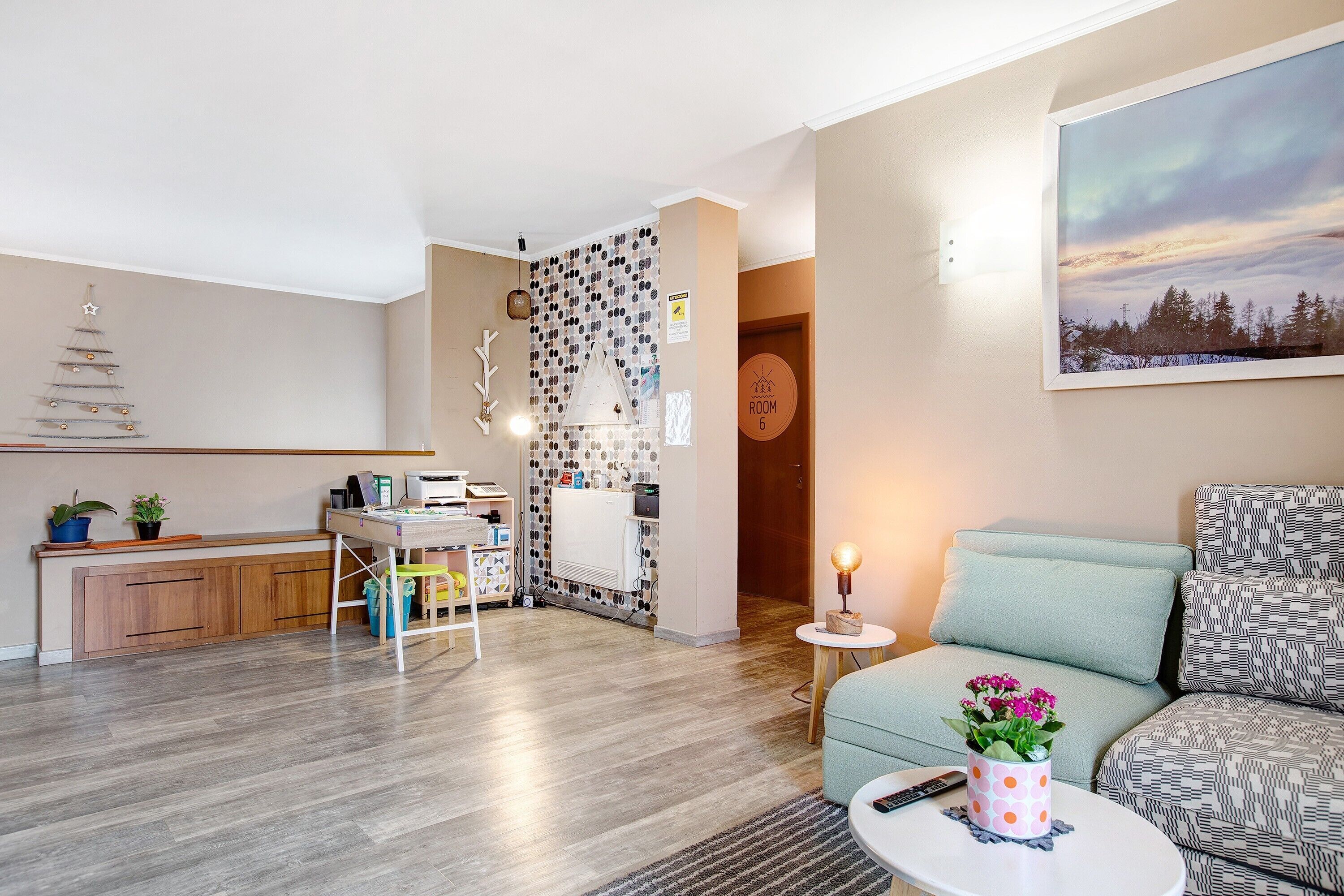 Ein modernes Wohnzimmer mit einer Couch, einem kleinen Tisch mit einer Pflanze, einer Küchenzeile mit einem Holzkasten und einer Wand mit einem gerahmten Bild.