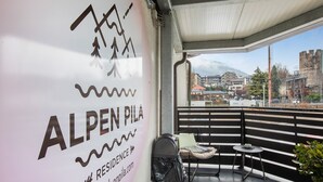 Een balkon met uitzicht op een stadslandschap, een bord met Alpen Pila en een afvalbak.