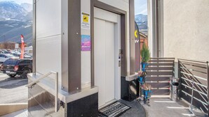 Een hotelentree met een deur, een welkomstmat, een prullenbak en uitzicht op bergen.