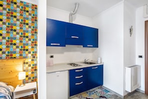 Uma cozinha compacta com armários azuis, geladeira branca e painel de fundo estampado.