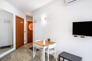 A room with a wooden table, white chairs, a small potted plant, a flat-screen TV mounted on the wall, and a door with a sign indicating the room number.