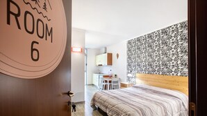 Un dormitorio con cama, escritorio y silla. Hay una pared con estampado floral y una puerta con la leyenda 'ROOM 6'.