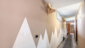 Un pasillo con diseño mural de temática montañosa, una planta en maceta y una puerta al final.