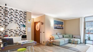 Una sala de estar moderna con un sofá, un escritorio con una computadora portátil, una mesita con una lámpara y una pared con un diseño geométrico.