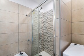 Une douche avec une porte en verre, un lavabo blanc et un mur carrelé.