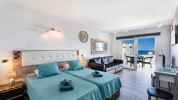 A hotel room with two beds, a sofa, a dining area, and a view of the sea. - Vacation Studio 'Las Flores 407' with Sea View, Shared Pool and Wi-Fi (Costa Adeje)