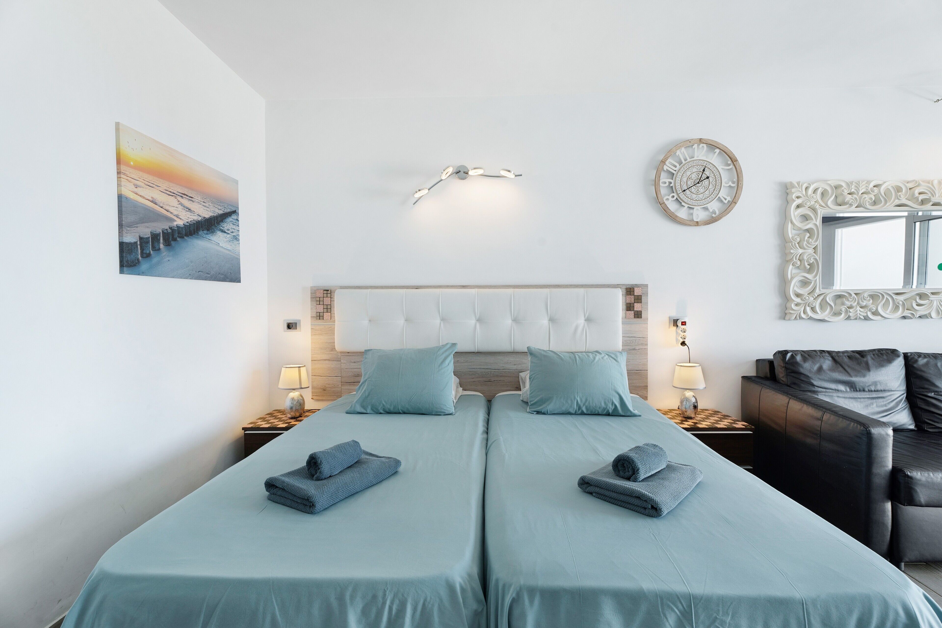 A double room with two beds, a headboard, bedside tables, lamps, a clock, a mirror, and a painting on the wall.