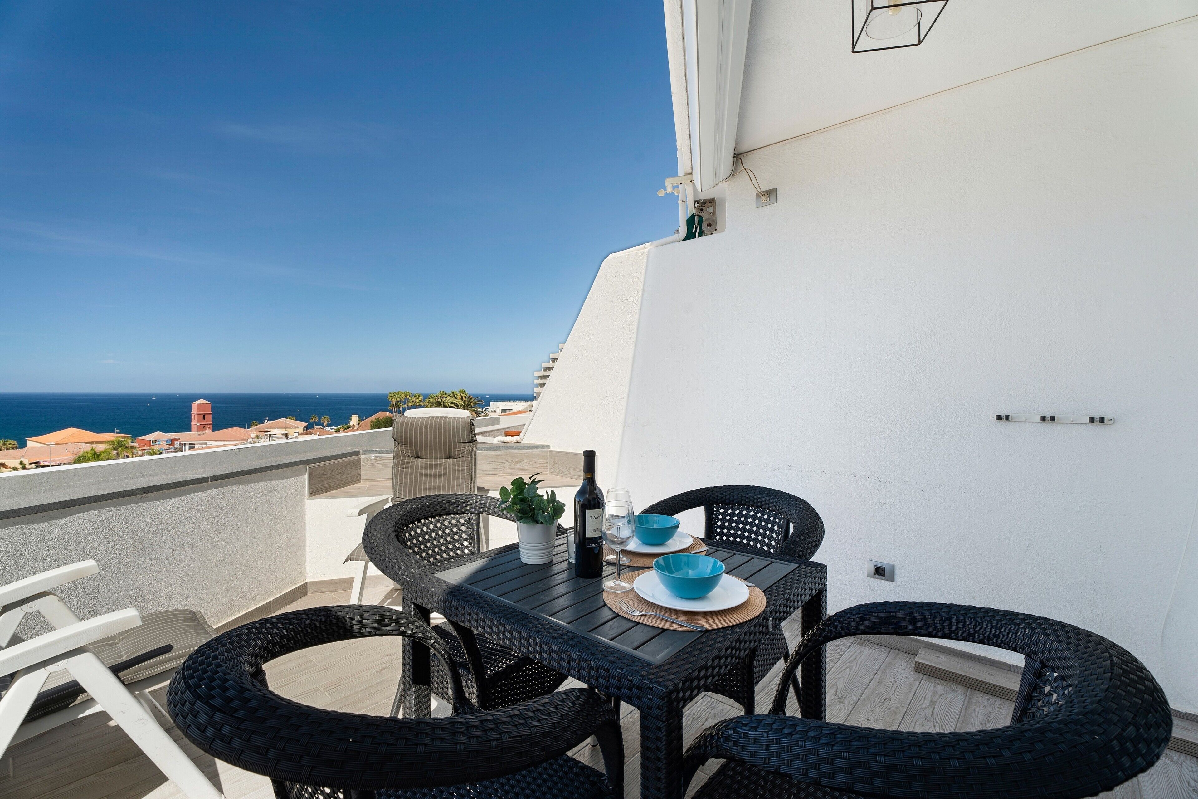 Un balcon avec une table dressée pour deux personnes, une bouteille de vin et une vue sur la mer.