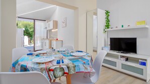 A dining area with a table set for four, a television on a stand, and a view of the outdoors. - Vacation Home "Sea Wave House" with Private Garden and Wi-Fi (San Teodoro)