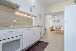 Une cuisine moderne avec des armoires blanches, un four encastré, une hotte de cuisinière en acier inoxydable et un coin repas comprenant une table et des chaises.