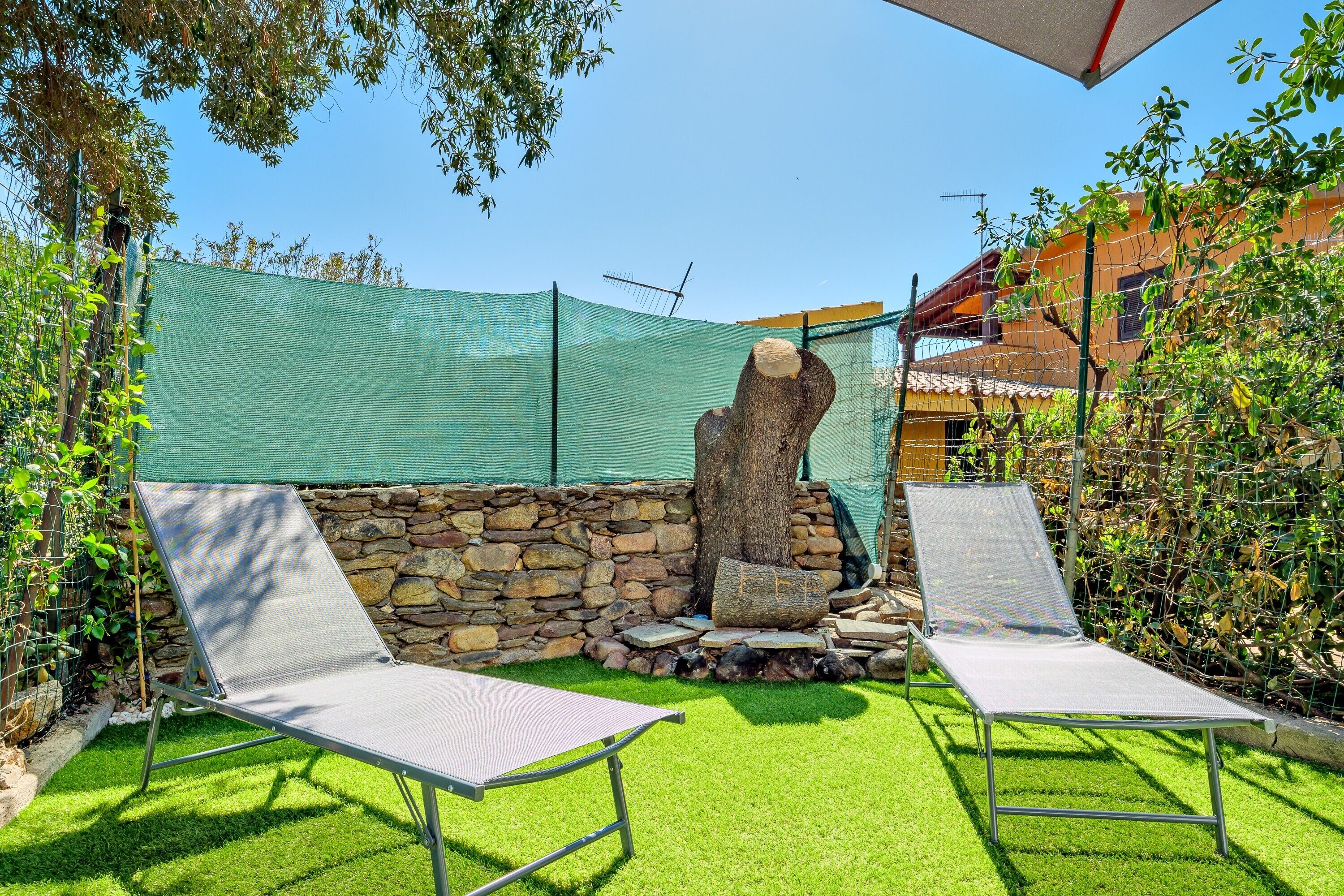 A patio with two lounge chairs, a stone wall, and a green netting structure.