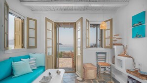 A room with a stone floor, a turquoise sofa, a white table, and a view of the sea through open doors. - Holiday Home 'Karavi' with Private Terrace, Balcony and Air Conditioning (S???f??)