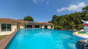 A swimming pool with a wooden deck, a house with a tiled roof, and trees in the background.