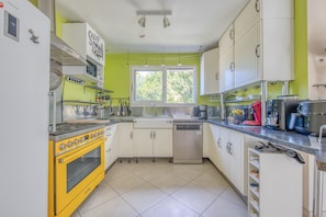 A kitchen with a yellow stove, white cabinets, a window, and a dishwasher.
