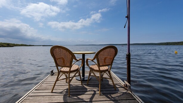 A wooden deck with two wicker chairs and a small round table, overlooking calm water.