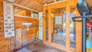 A wooden cabin interior with a wooden floor, a sink, a shower area, and a door leading outside.