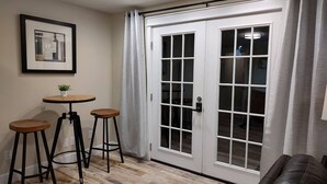 A room with a wooden floor, a white door with glass panels, two stools, a small table with a plant, and a framed picture on the wall. - Cozy Harborside Condo, Florence (Florence)
