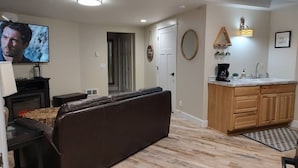 A living room with a brown leather sofa, a TV, a fireplace, and a wooden floor. - Cozy Harborside Condo, Florence (Florence)