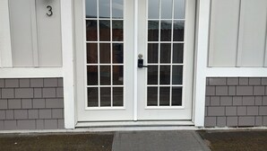 A white double door with a glass panel, a number '3' above it, and a small outdoor light fixture to the left. - Cozy Harborside Condo, Florence (Florence)