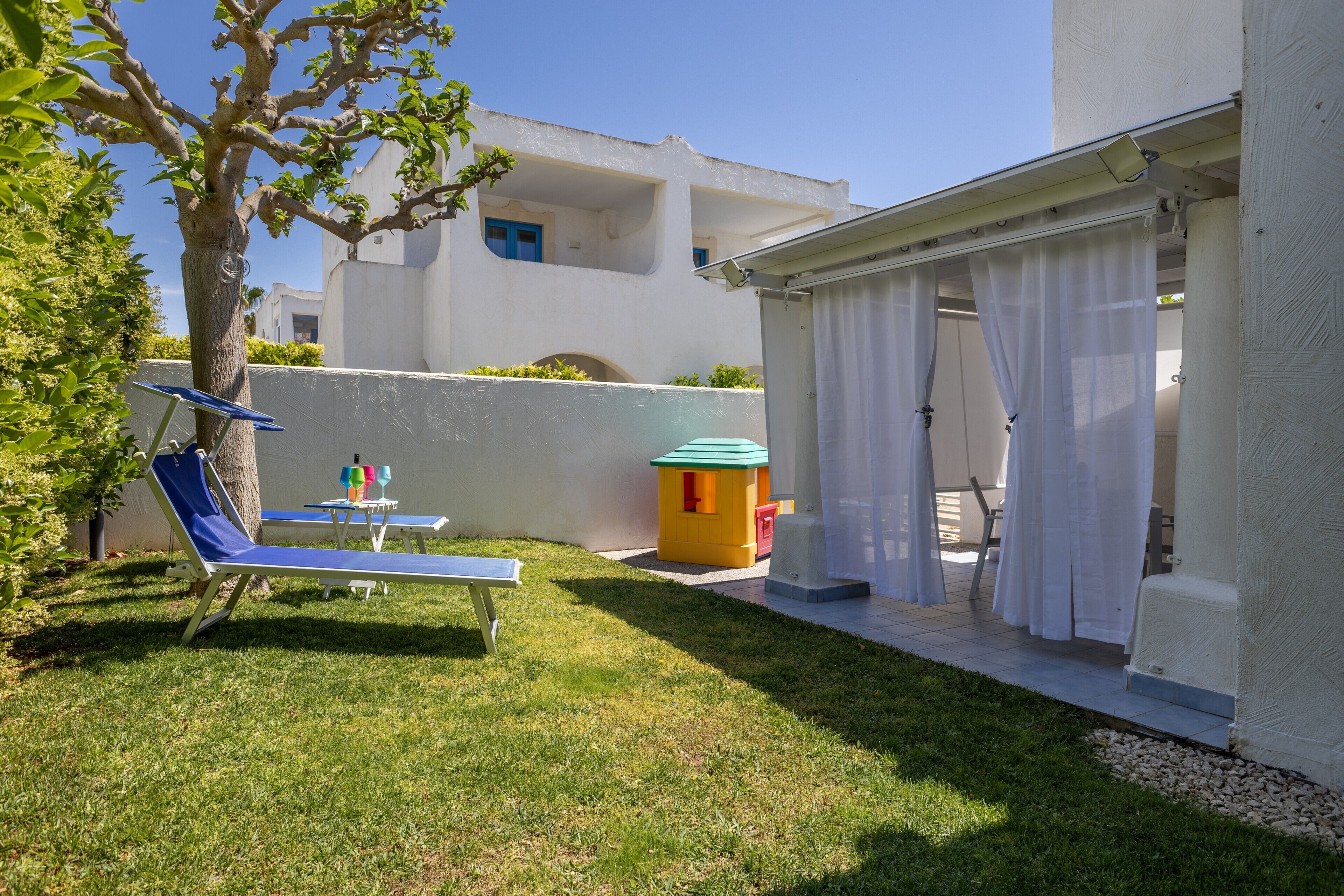 A covered outdoor area with a table and chairs, a small playhouse, and a tree.
