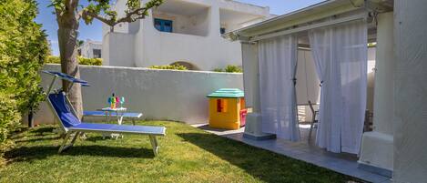 A covered outdoor area with a table and chairs, a small playhouse, and a tree.