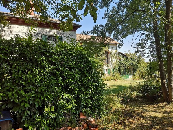 A garden with a white building, green foliage, and a clear sky. - Cottage 'Cascina Risotto' with private pool, Wi-Fi and air conditioning (Montaldo Bormida)