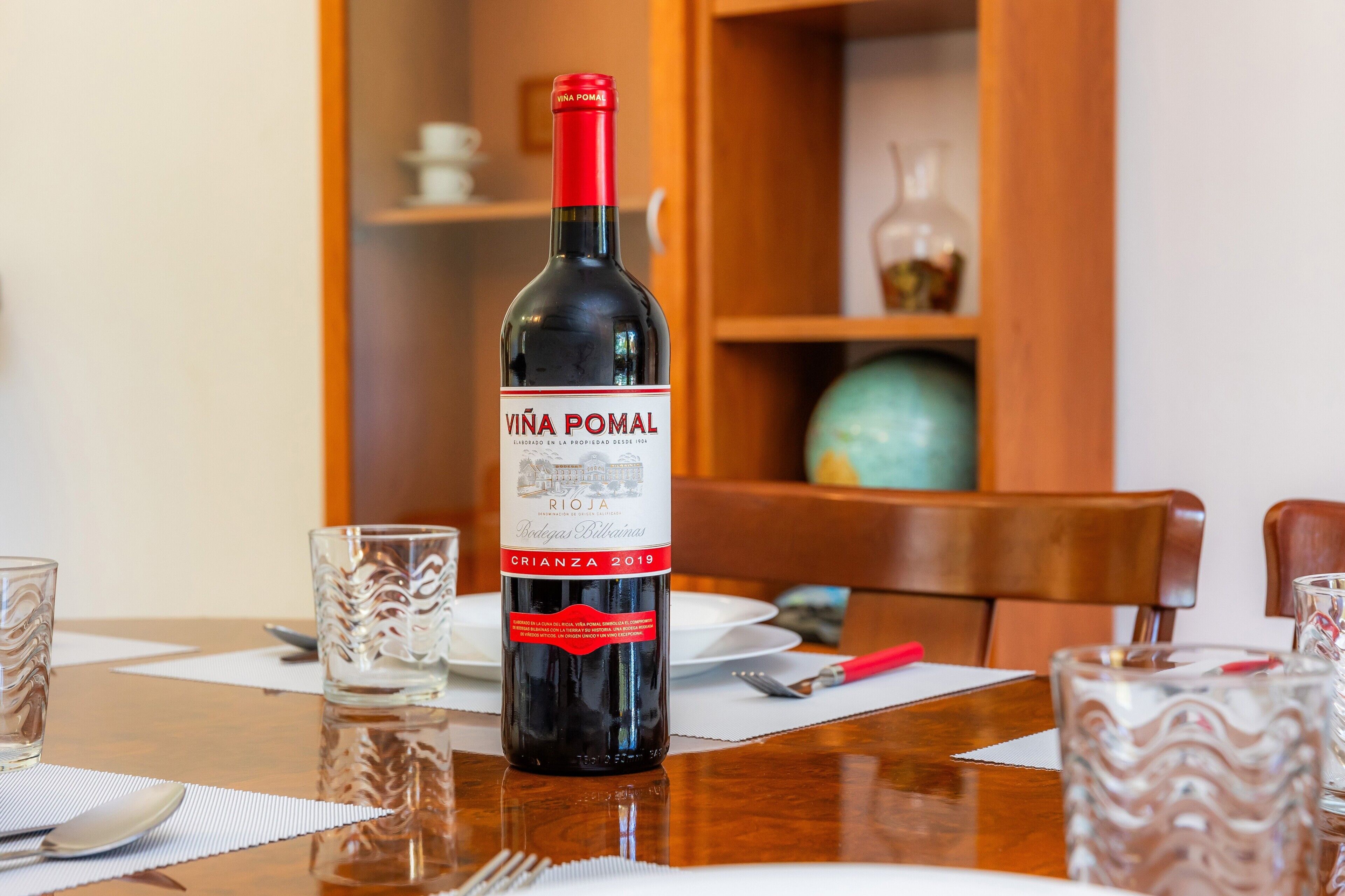 Una bottiglia di vino su un tavolo con tovaglietta, un bicchiere e un cucchiaio.
