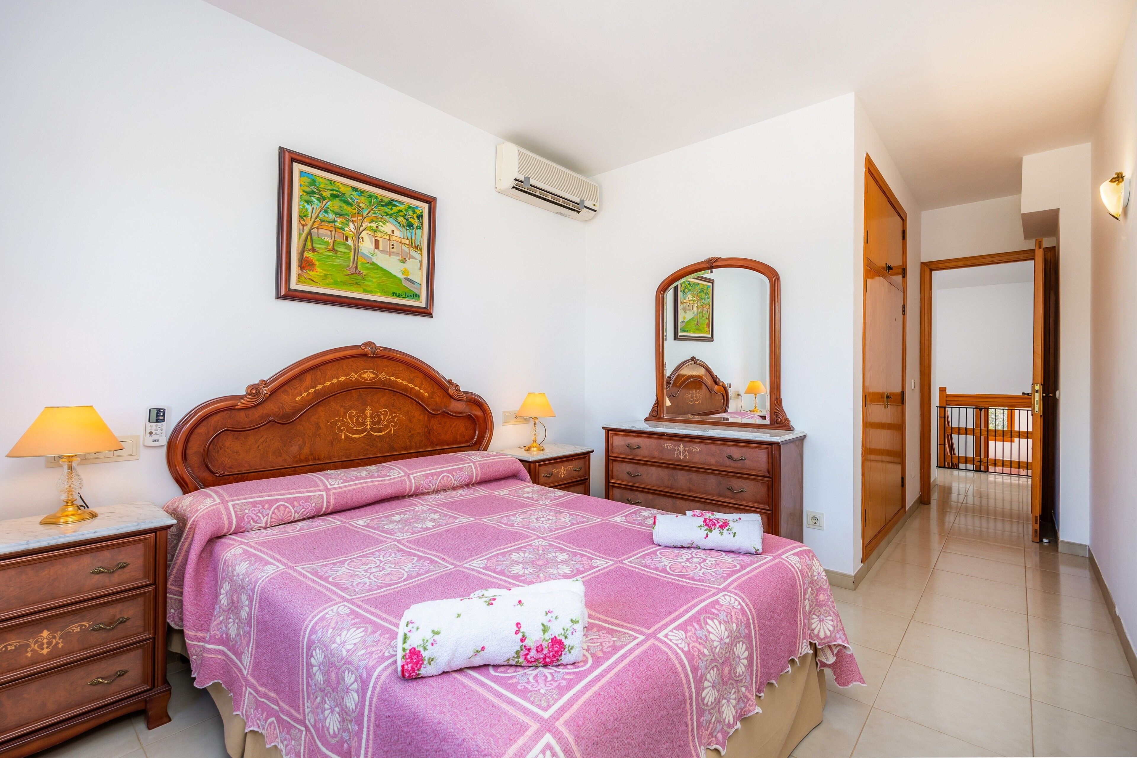 A bedroom with a bed, bedside tables, a dresser, a mirror, and a door leading to another room.