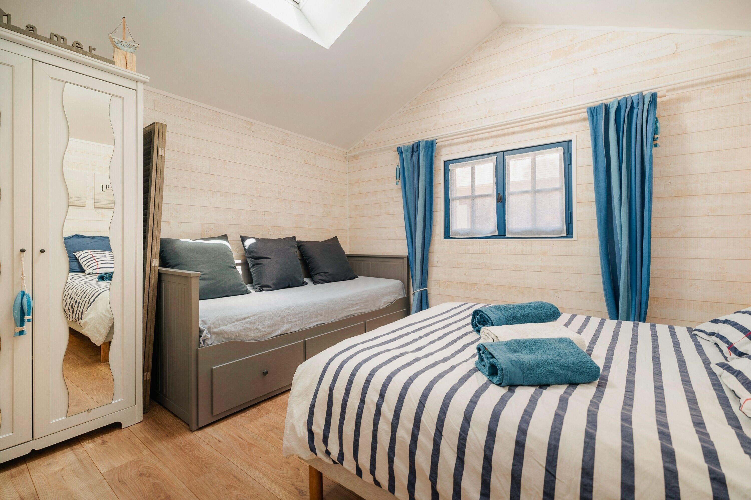 Ein Schlafzimmer mit einem Bett, einem Kleiderschrank, einem Fenster mit Vorhängen und einem Oberlicht.