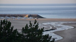 A coastal area with boats docked, a rocky outcrop, and a sandy beach. - Cottage 'Gîte La Marinière' with Private Terrace and Private Garden (Plurien)