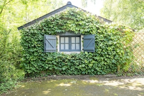 A small house with a window and shutters, surrounded by dense green foliage.