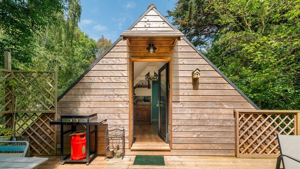 Una cabaña de madera con techo triangular, una puerta y un pequeño porche.