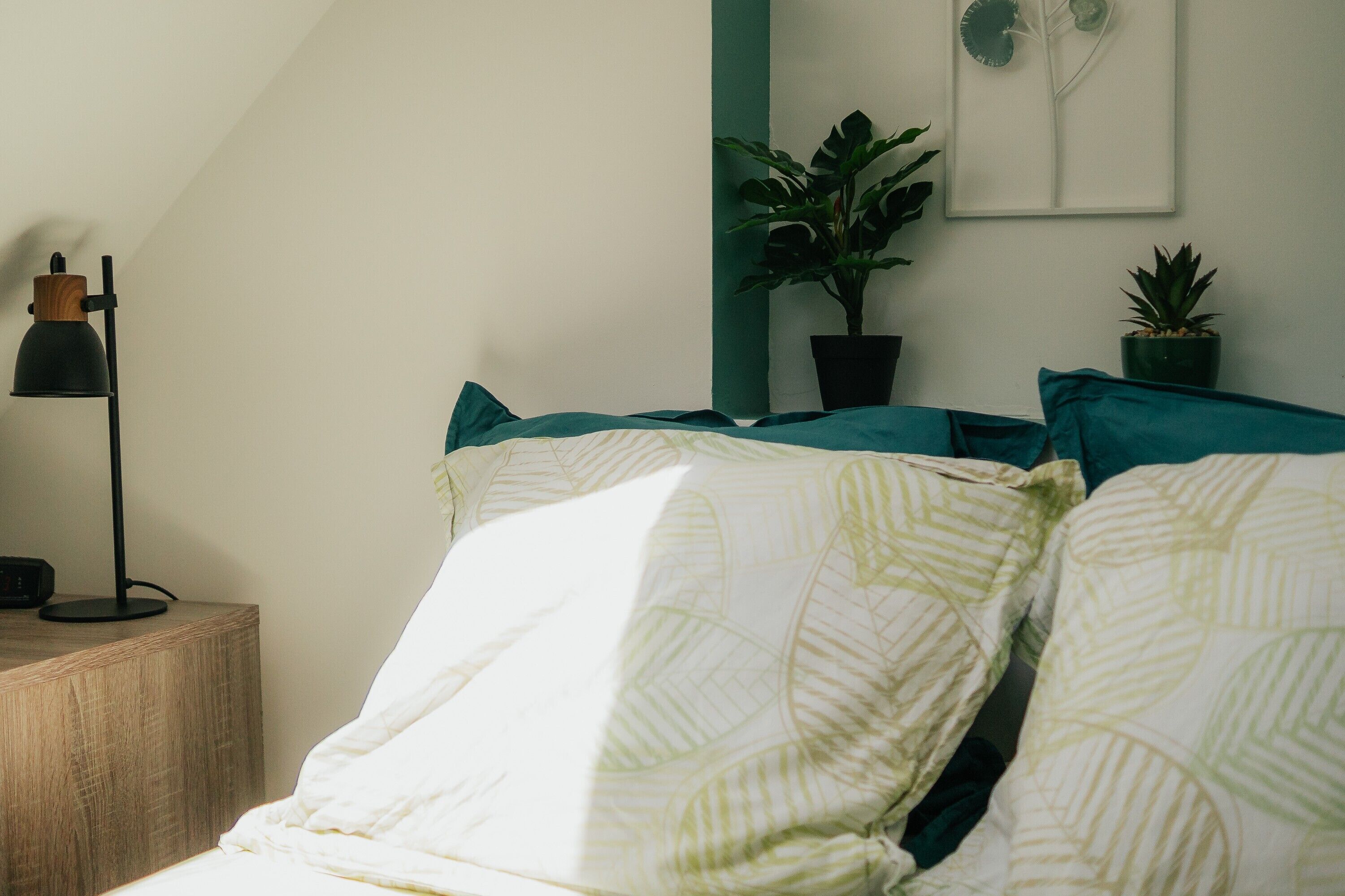 A bedroom with a bed, a bedside table, a lamp, and two potted plants.