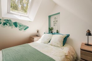 Quarto com cama, mesa de cabeceira, luminária, janela e um objeto decorativo na parede.