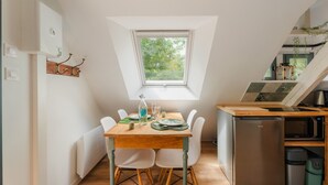 Cocina compacta con mesa, sillas, refrigerador y ventana con vista a zonas verdes.