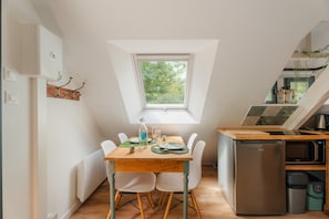 Cocina compacta con mesa, sillas, refrigerador y ventana con vista a zonas verdes.